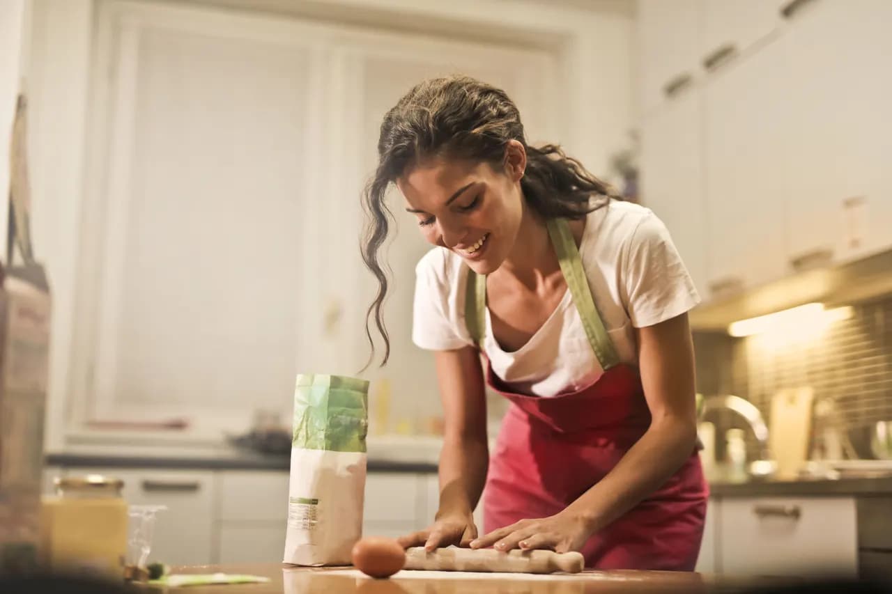 A woman in an apron rolling out dough on her kitchen counter
